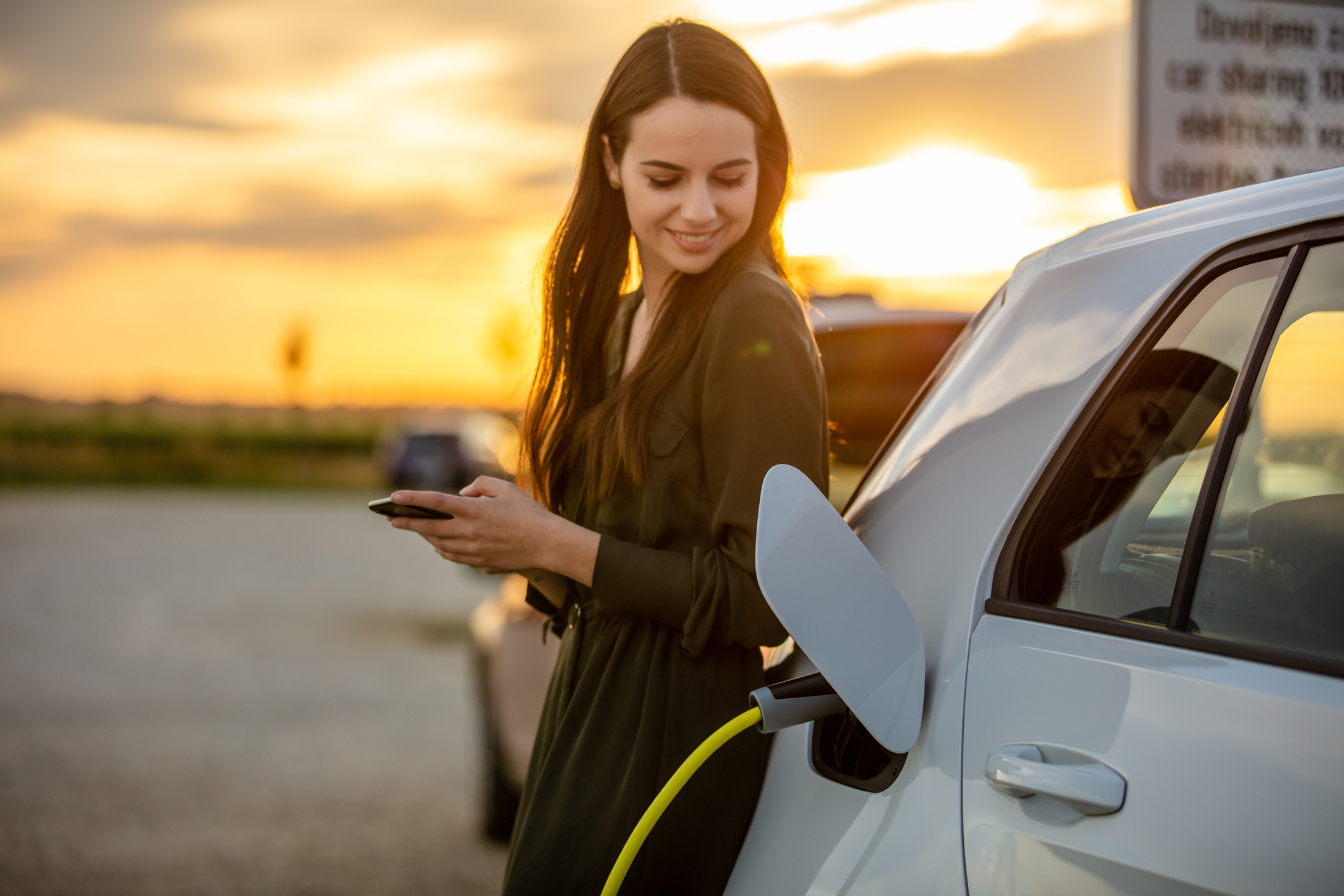 Woman with sunset behind her charging her EV